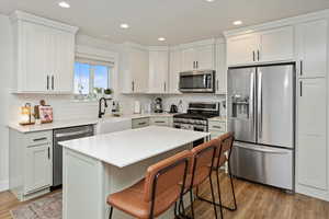 Kitchen with hardwood / wood-style floors, a center island, a breakfast bar, appliances with stainless steel finishes, and white cabinets