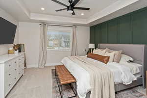 Bedroom with ceiling fan, light colored carpet, and a raised ceiling