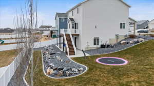 Rear view of property with a trampoline, a deck, cooling unit, and a yard