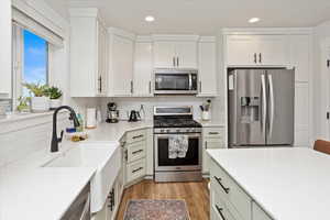 Kitchen with light stone countertops, white cabinets, appliances with stainless steel finishes, decorative backsplash, and light hardwood / wood-style flooring