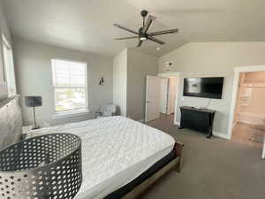 Bedroom featuring vaulted ceiling, ceiling fan, carpet flooring, and ensuite bath