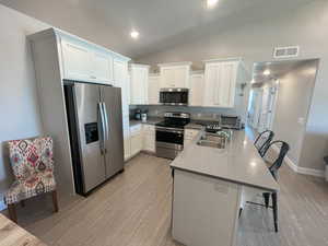 Kitchen featuring a breakfast bar area, appliances with stainless steel finishes, white cabinets, and sink