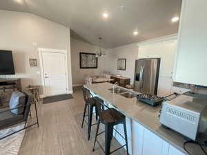 Kitchen featuring pendant lighting, white cabinets, stainless steel fridge with ice dispenser, a notable chandelier, and vaulted ceiling