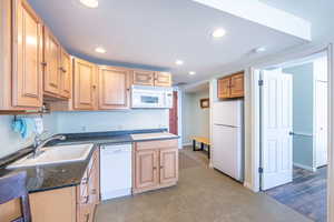 Kitchen with sink, white appliances, a textured ceiling, and dark stone countertops