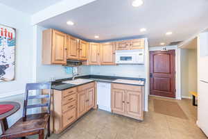 Kitchen with white appliances, light brown cabinets, sink, and light tile patterned floors