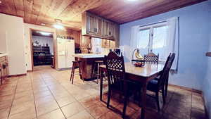 Dining space with ceiling fan, sink, light tile patterned floors, and wood ceiling