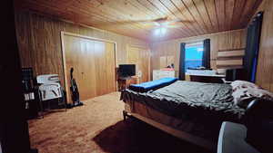 Carpeted bedroom with ceiling fan, wood ceiling, wood walls, and multiple closets