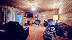 Carpeted living room featuring wooden ceiling, a wood stove, ceiling fan, and wooden walls