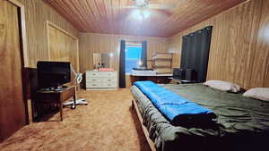 Carpeted bedroom featuring ceiling fan, wood ceiling, and wood walls