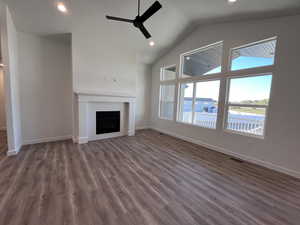 Unfurnished living room with ceiling fan, a water view, dark wood-type flooring, and lofted ceiling