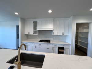 Kitchen with white cabinets, tasteful backsplash, sink, light stone counters, and gas stovetop