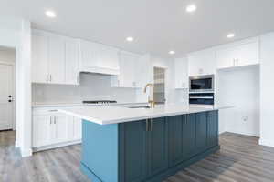 Kitchen with built in microwave, white cabinetry, and a center island with sink