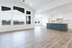 Unfurnished living room featuring ceiling fan, high vaulted ceiling, sink, and light wood-type flooring