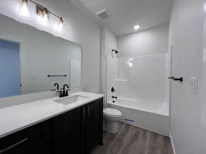 Full bathroom with toilet, vanity, washtub / shower combination, and hardwood / wood-style flooring