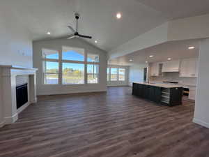 Unfurnished living room featuring ceiling fan, dark wood-type flooring, sink, and high vaulted ceiling