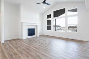 Unfurnished living room featuring ceiling fan, a fireplace, high vaulted ceiling, and light wood-type flooring