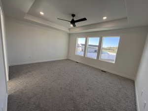 Carpeted spare room with ceiling fan and a tray ceiling