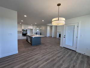 Kitchen with decorative light fixtures, oven, a center island with sink, sink, and white cabinets