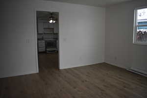 Empty room featuring ceiling fan, a baseboard heating unit, and dark wood-type flooring