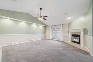 Unfurnished living room featuring ceiling fan, carpet, and lofted ceiling