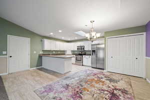 Kitchen with decorative light fixtures, kitchen peninsula, an inviting chandelier, appliances with stainless steel finishes, and white cabinets