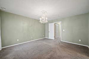 Carpeted spare room featuring a textured ceiling and a chandelier