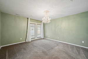 Unfurnished room featuring carpet, a notable chandelier, and a textured ceiling