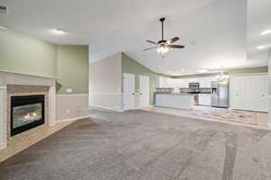 Unfurnished living room with lofted ceiling, light carpet, a fireplace, and ceiling fan with notable chandelier