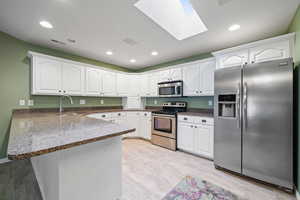 Kitchen featuring white cabinets, kitchen peninsula, a skylight, and stainless steel appliances