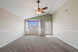 Carpeted empty room with ceiling fan, vaulted ceiling, and a textured ceiling