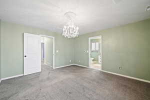 Carpeted spare room featuring a notable chandelier and a textured ceiling