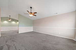 Spare room featuring vaulted ceiling, ceiling fan, and carpet flooring