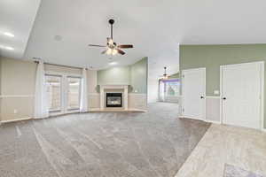 Unfurnished living room featuring ceiling fan, vaulted ceiling, and light carpet