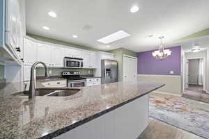 Kitchen with pendant lighting, white cabinetry, stainless steel appliances, and dark stone countertops