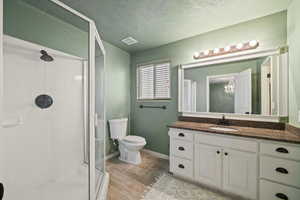 Bathroom with a textured ceiling, toilet, walk in shower, and vanity