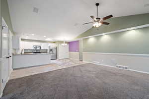 Unfurnished living room featuring vaulted ceiling, light colored carpet, ceiling fan with notable chandelier, and sink