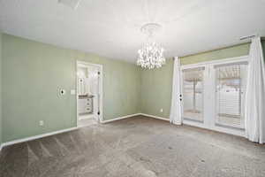 Unfurnished room featuring a textured ceiling, an inviting chandelier, and carpet