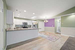 Kitchen with white cabinetry, kitchen peninsula, stainless steel appliances, decorative light fixtures, and a chandelier