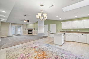 Kitchen featuring ceiling fan with notable chandelier, white cabinetry, sink, hanging light fixtures, and lofted ceiling with skylight