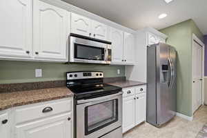 Kitchen featuring white cabinets, appliances with stainless steel finishes, and dark stone counters