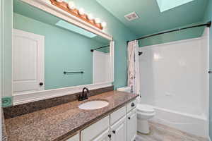 Full bathroom with toilet, vanity, shower / bath combo, a skylight, and a textured ceiling