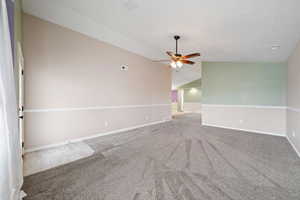 Spare room featuring vaulted ceiling, ceiling fan, a textured ceiling, and carpet floors