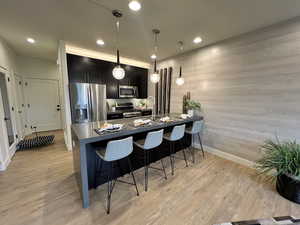 Kitchen with decorative light fixtures, sink, light wood-type flooring, a breakfast bar area, and stainless steel appliances