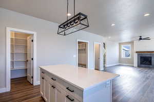 Kitchen with white cabinets, a kitchen island, decorative light fixtures, ceiling fan, and a tiled fireplace