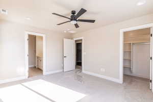 Unfurnished bedroom featuring a walk in closet, connected bathroom, a closet, ceiling fan, and light colored carpet