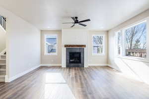 Unfurnished living room with ceiling fan, wood-type flooring, and a tiled fireplace