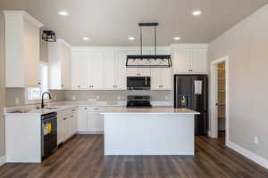 Kitchen featuring a center island, black appliances, sink, hanging light fixtures, and white cabinets