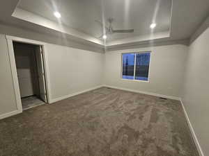 Empty room with ceiling fan, a tray ceiling, and carpet floors