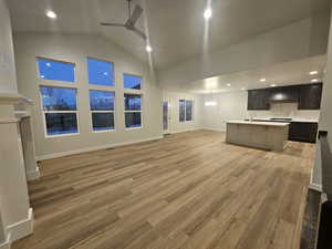 Unfurnished living room with high vaulted ceiling, light hardwood / wood-style floors, sink, and ceiling fan with notable chandelier