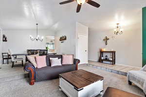 Living room with carpet, ceiling fan with notable chandelier, a textured ceiling, and lofted ceiling